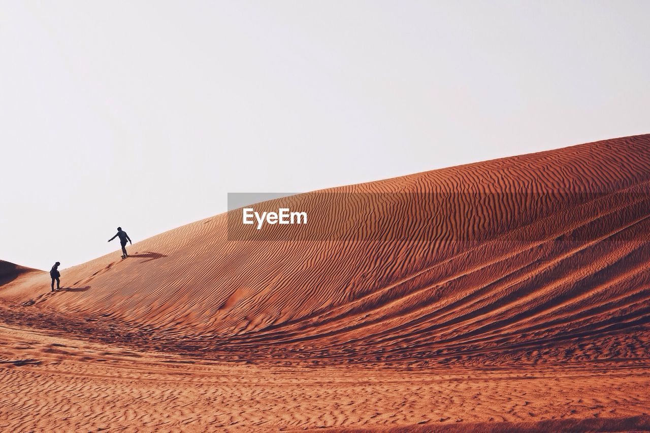 People on sand dune in dessert against clear sky