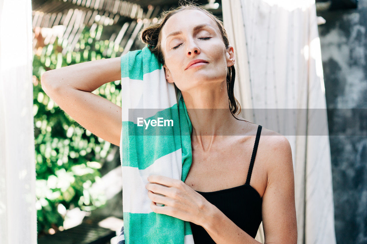 Close portrait of a woman drying her hair after a cool shower in the summer outside in the garden.