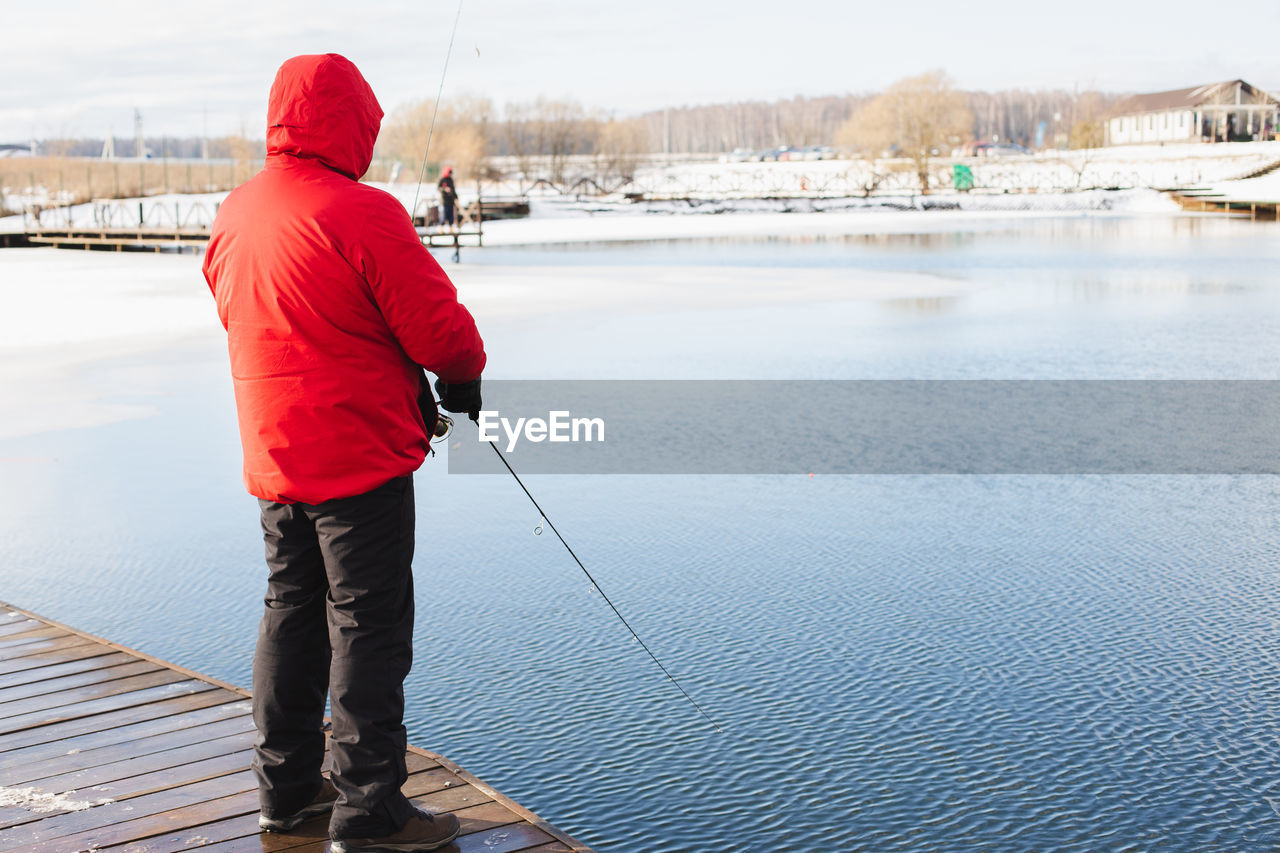 REAR VIEW OF MAN LOOKING AT LAKE