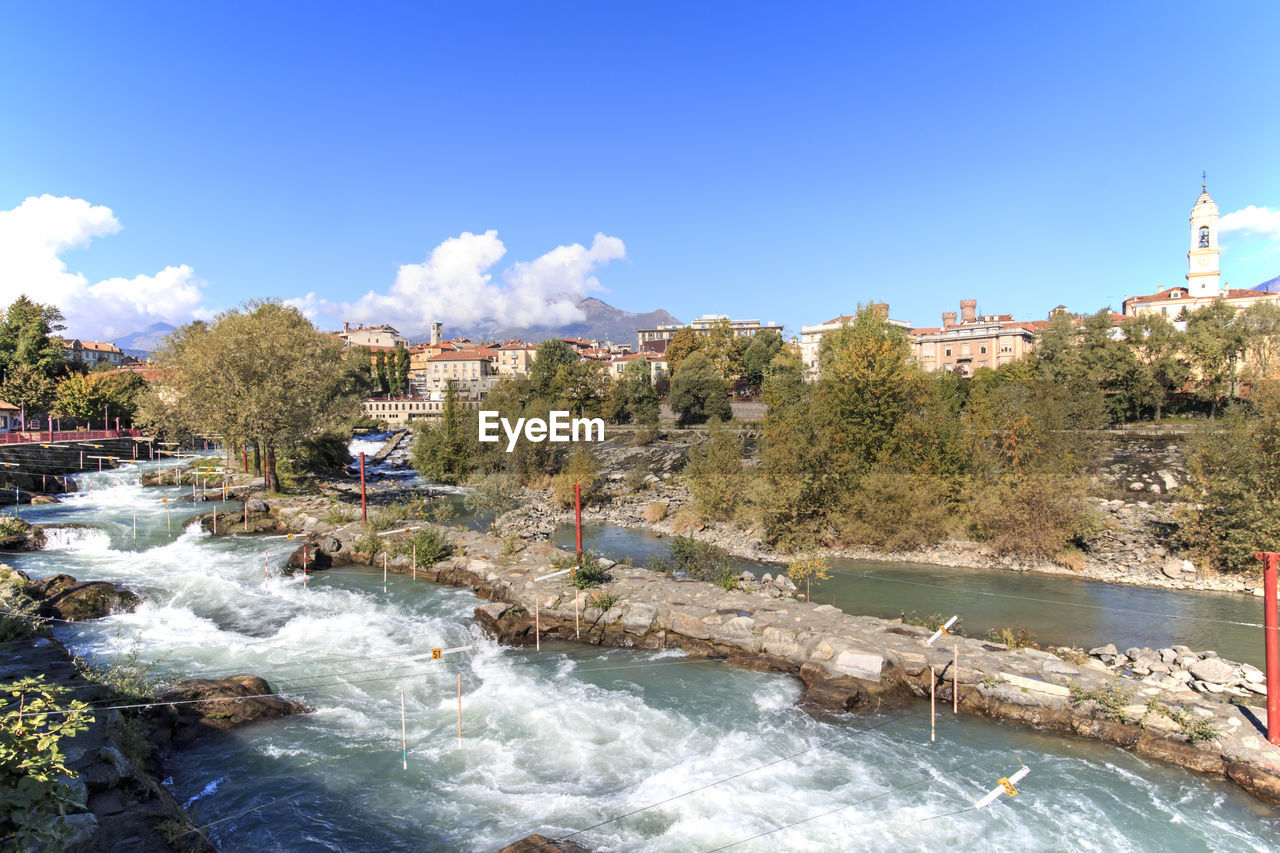 Scenic view of dora baltea river in city against blue sky