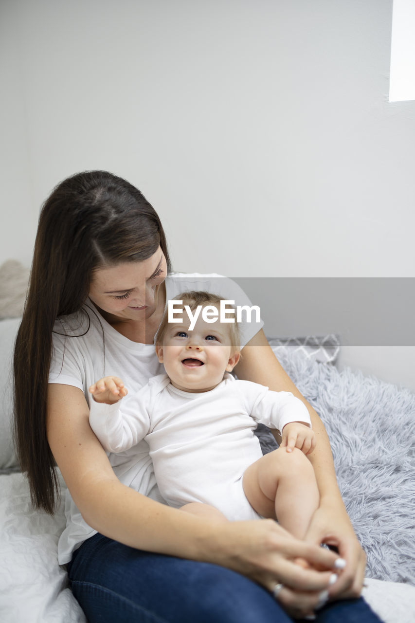 portrait of happy mother and daughter sitting on bed at home