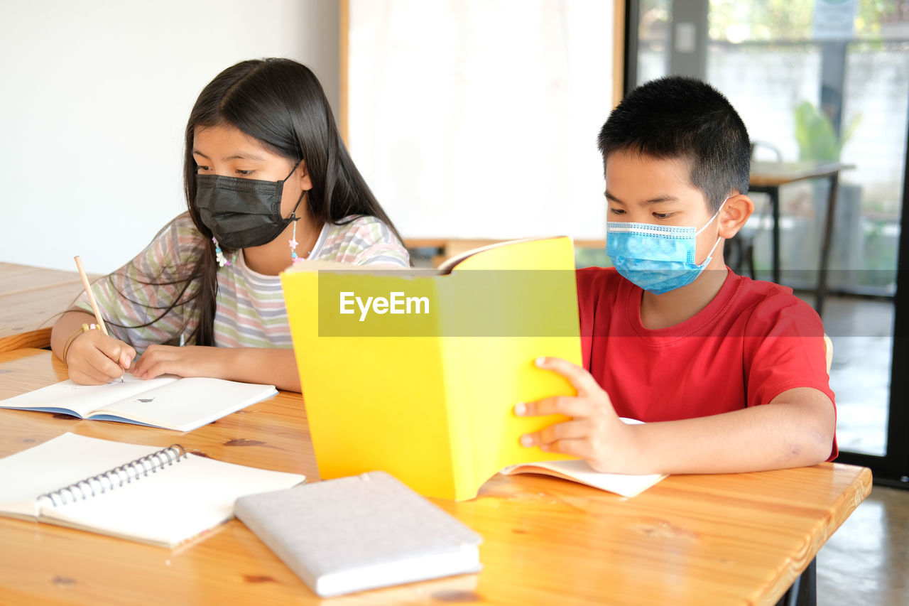 Asian girl boy student wearing face mask studying writing notes doing homework in library. learning