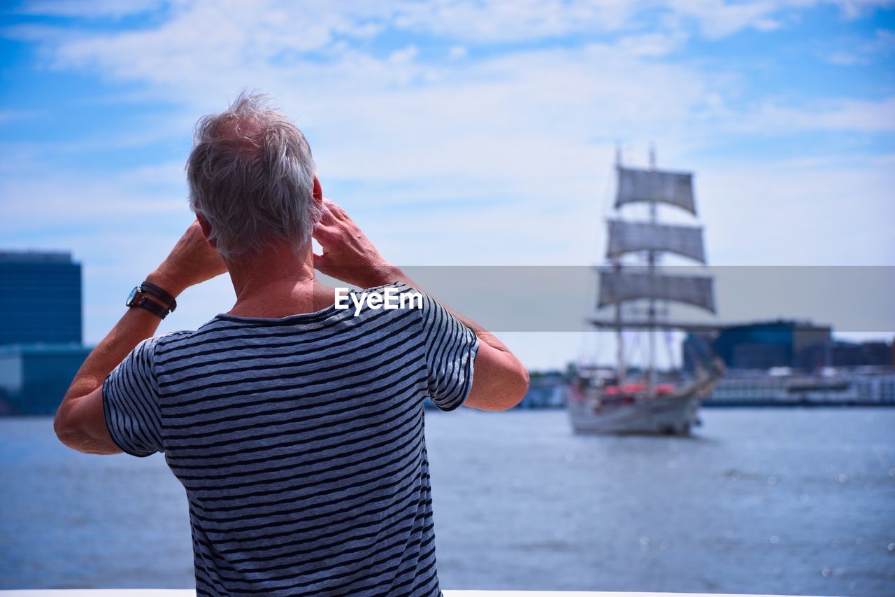 Rear view of man standing in harbor against sky