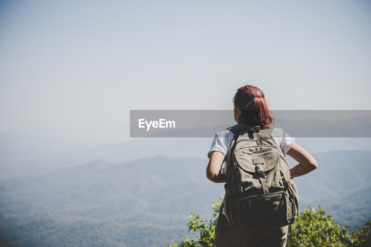 Rear view of backpack woman looking at mountains against sky