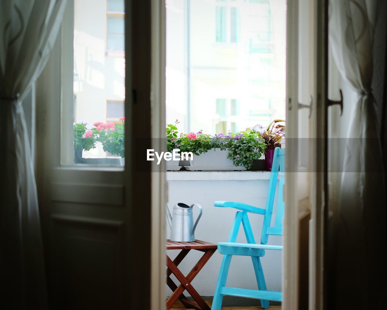 Chair and flower pots on balcony seen from partially opened door