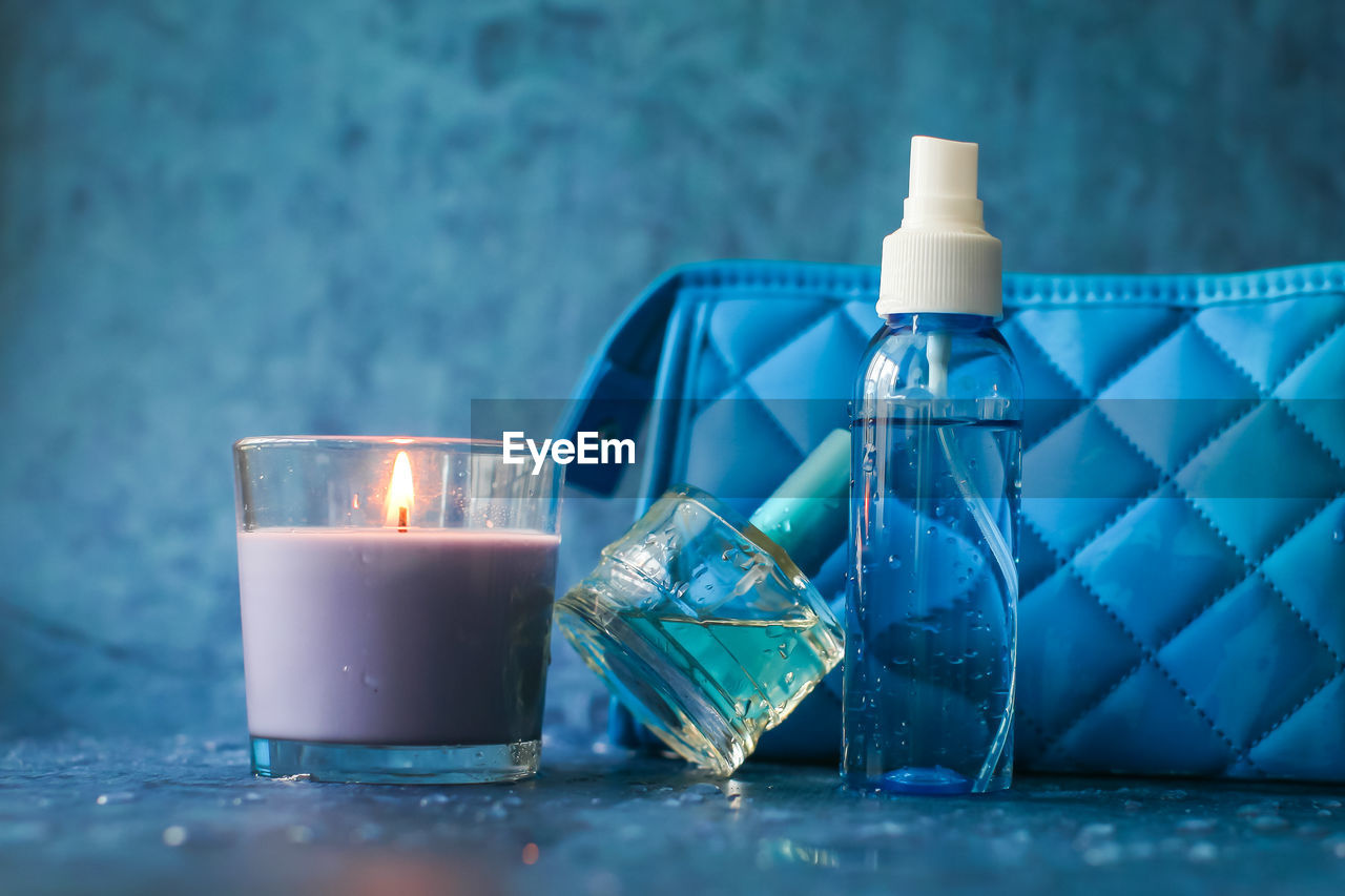 Close-up of small spray bottle with clutch bag and candle on blue table