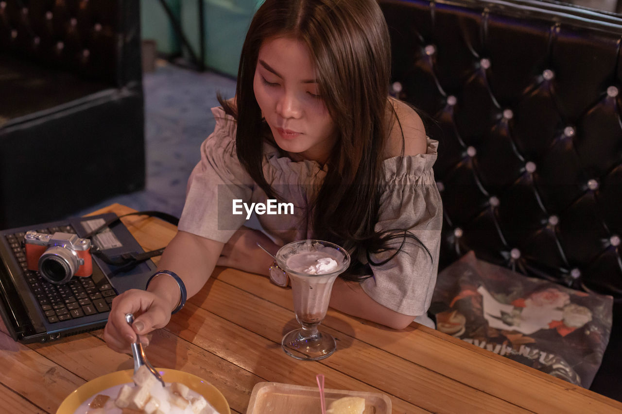 YOUNG WOMAN USING MOBILE PHONE WHILE SITTING AT TABLE