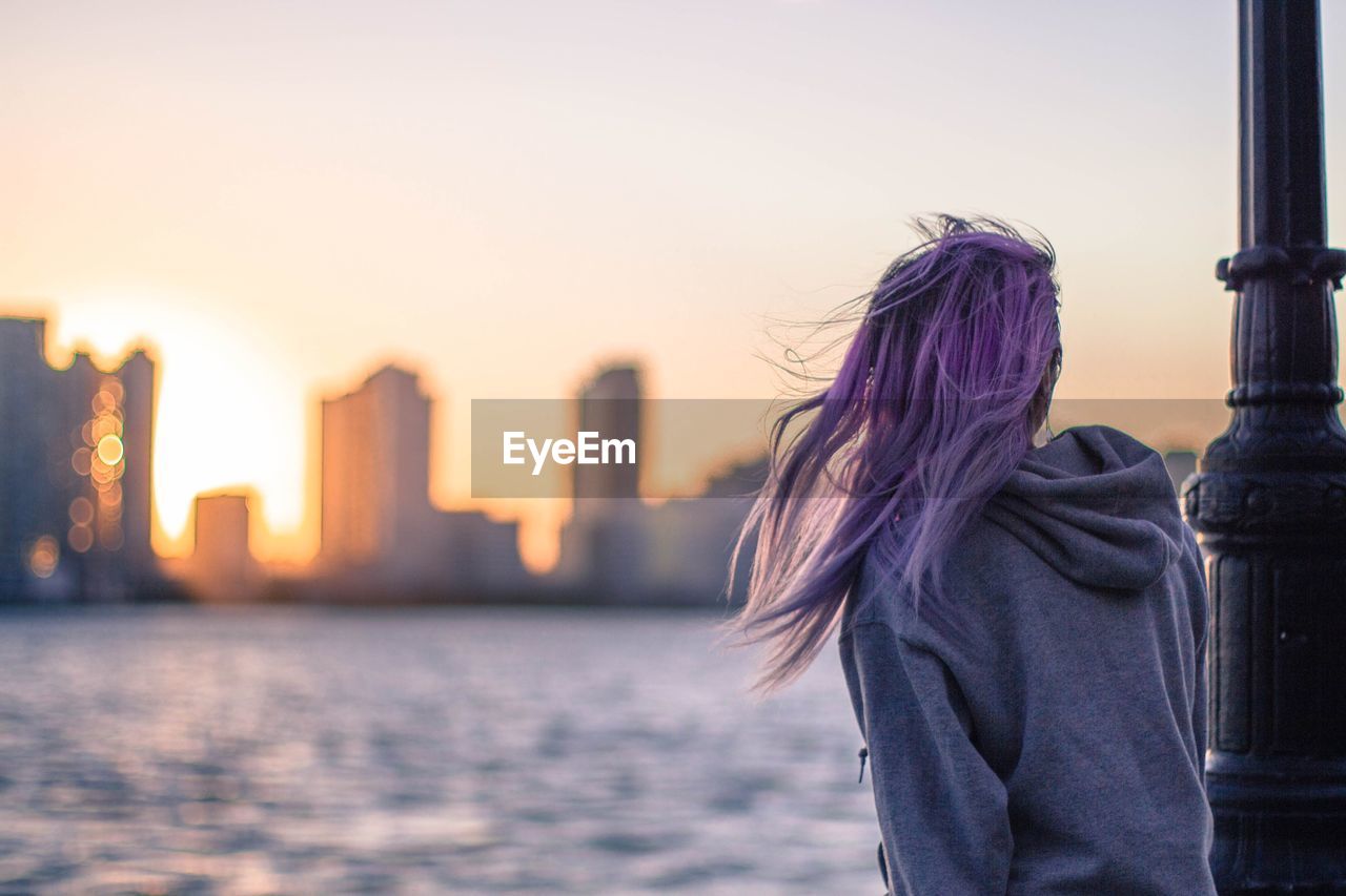 Rear view of young woman standing by sea against sky during sunset