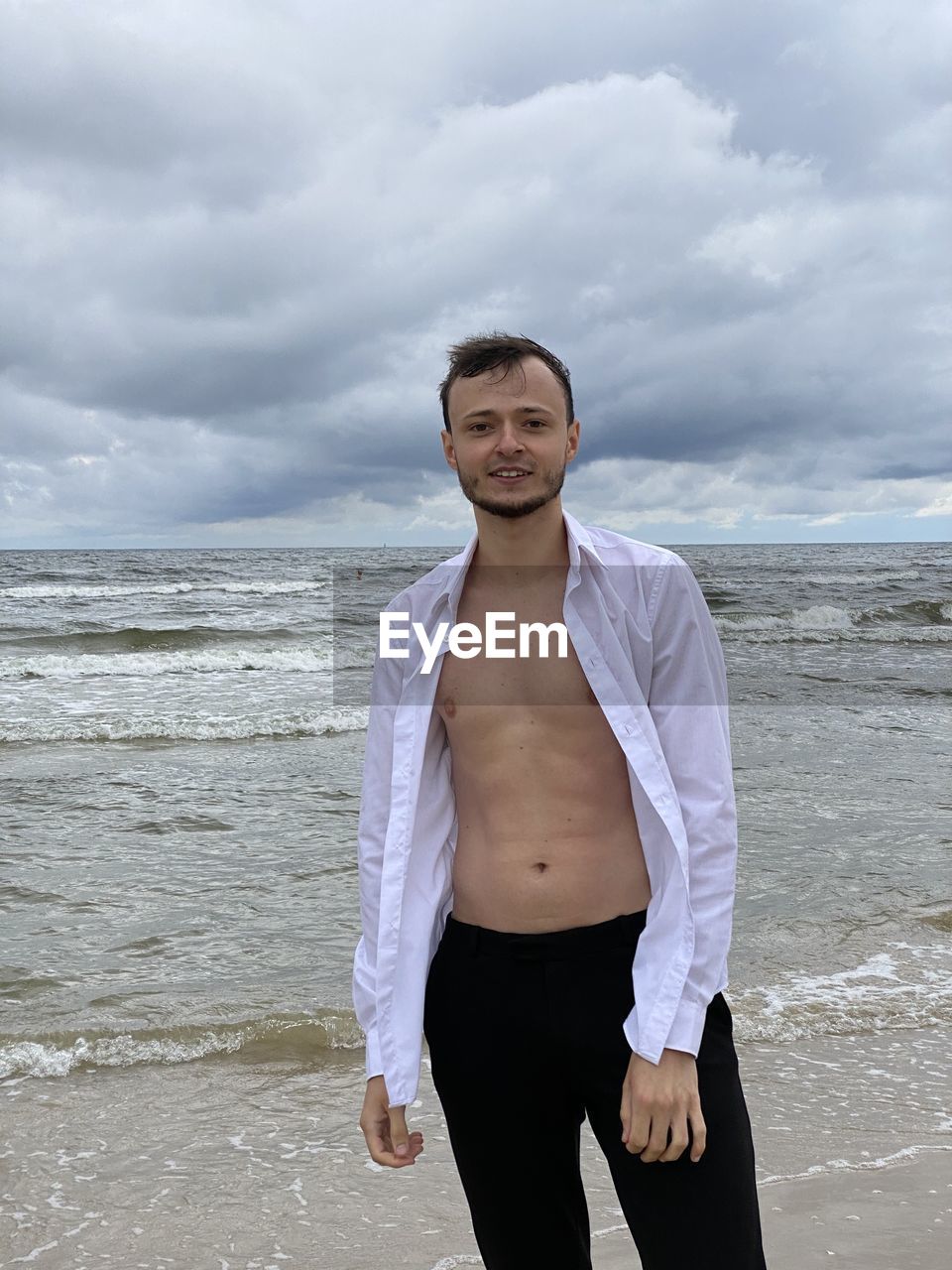 PORTRAIT OF YOUNG MAN STANDING AT BEACH