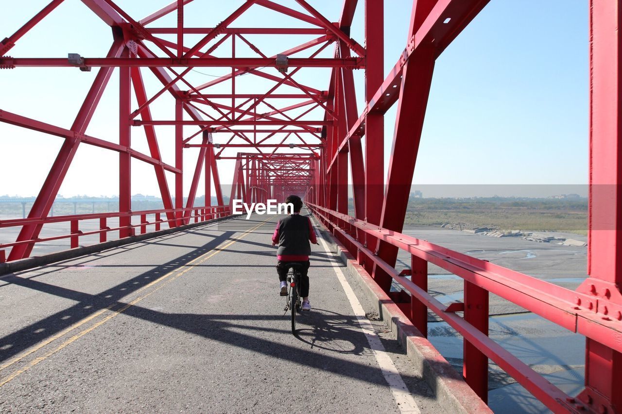 Rear view of man riding a bike on bridge over sea against clear sky