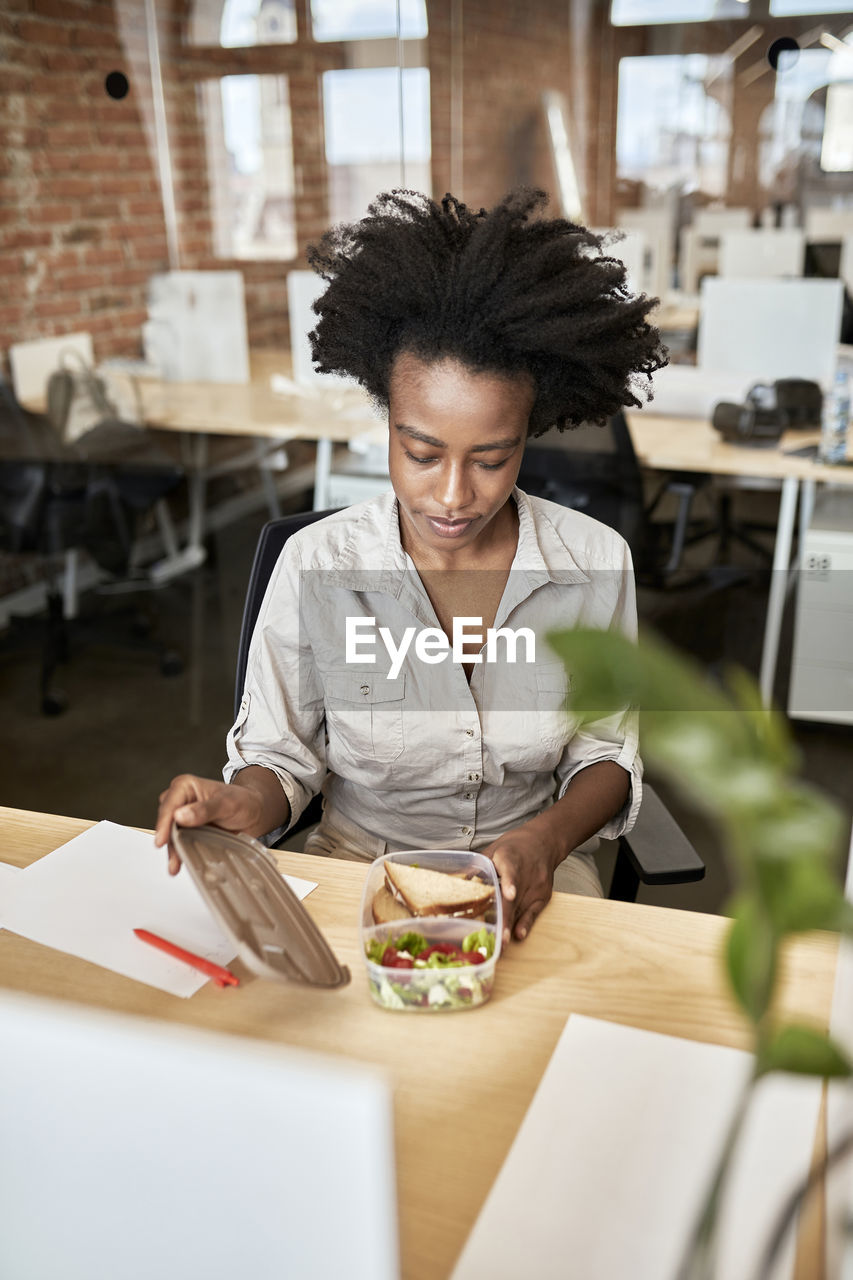 Afro businesswoman opening container during lunch break at office