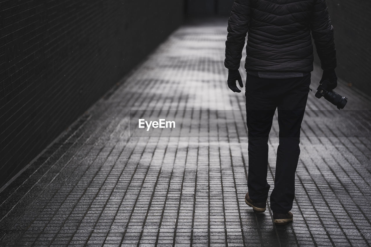 Low section of man walking on footpath with camera