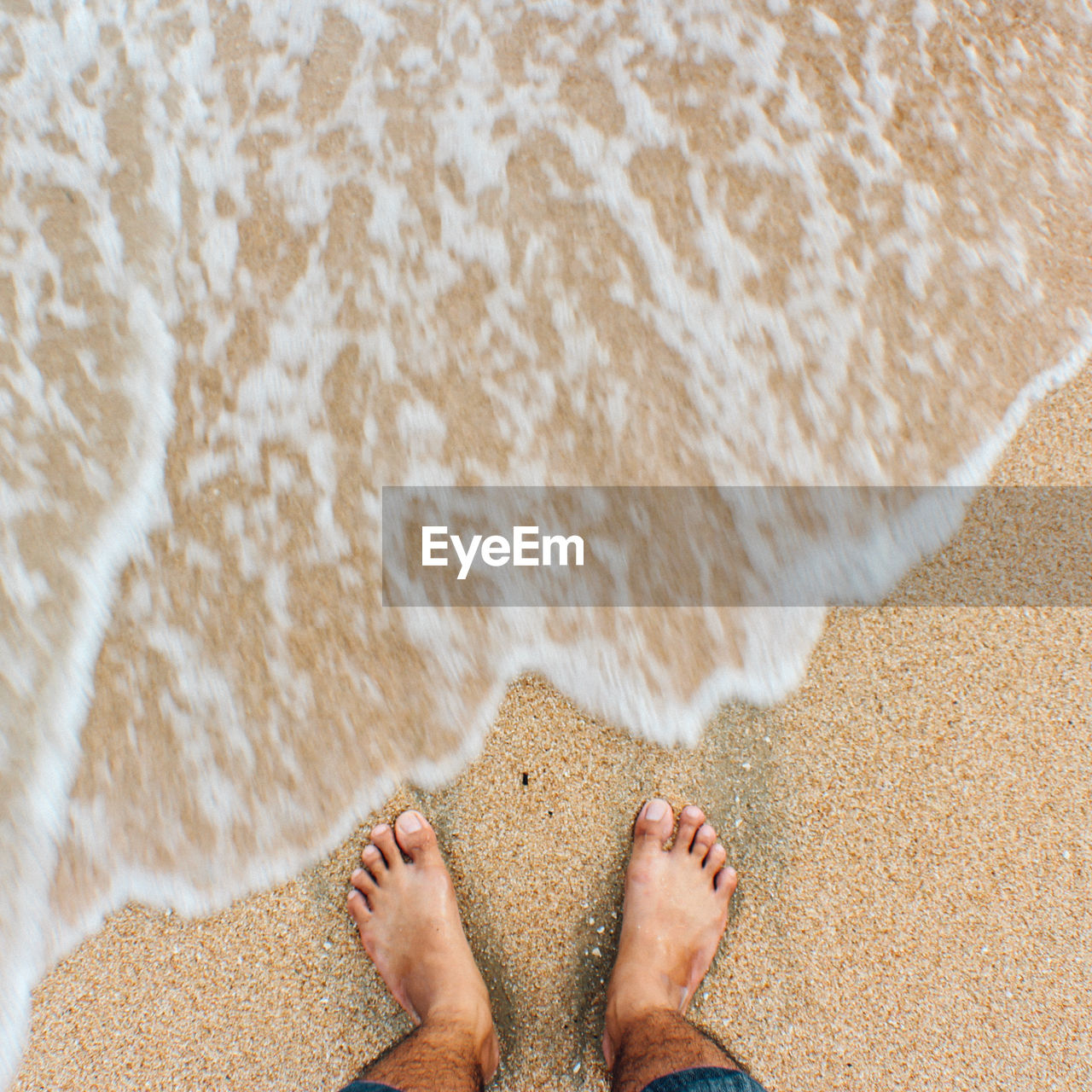 LOW SECTION OF PERSON STANDING ON SAND AT BEACH