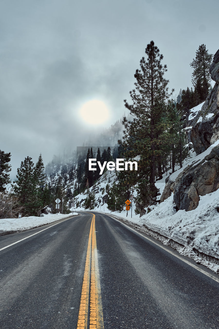 EMPTY ROAD ALONG SNOW COVERED LANDSCAPE