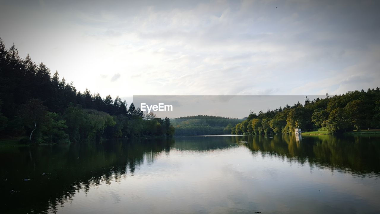 Scenic view of calm river with trees reflection against sky