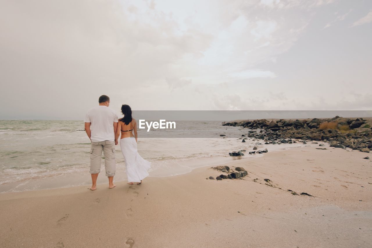 Couple walking at beach against sky