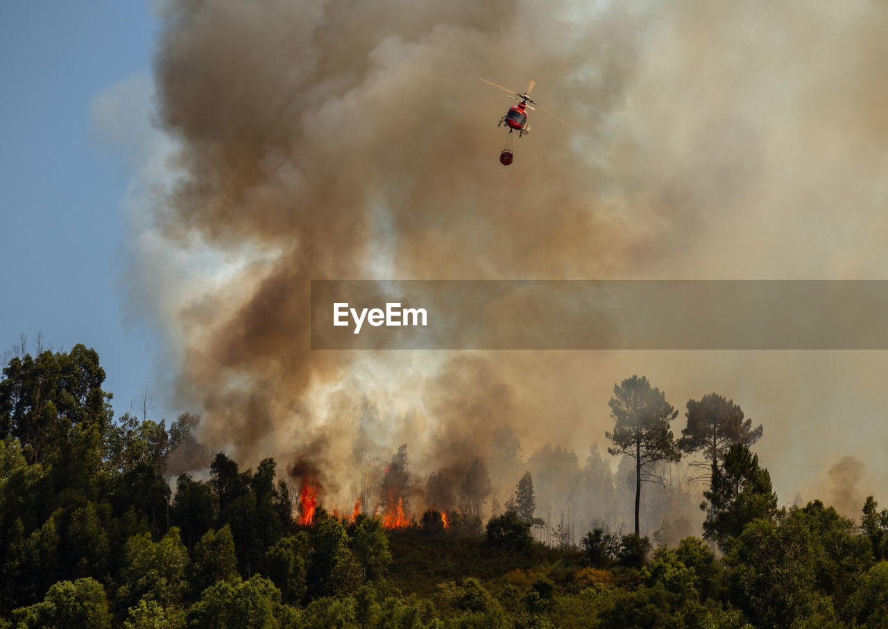 Firefighter helicopter fighting against a forest fire during day in braga, portugal.