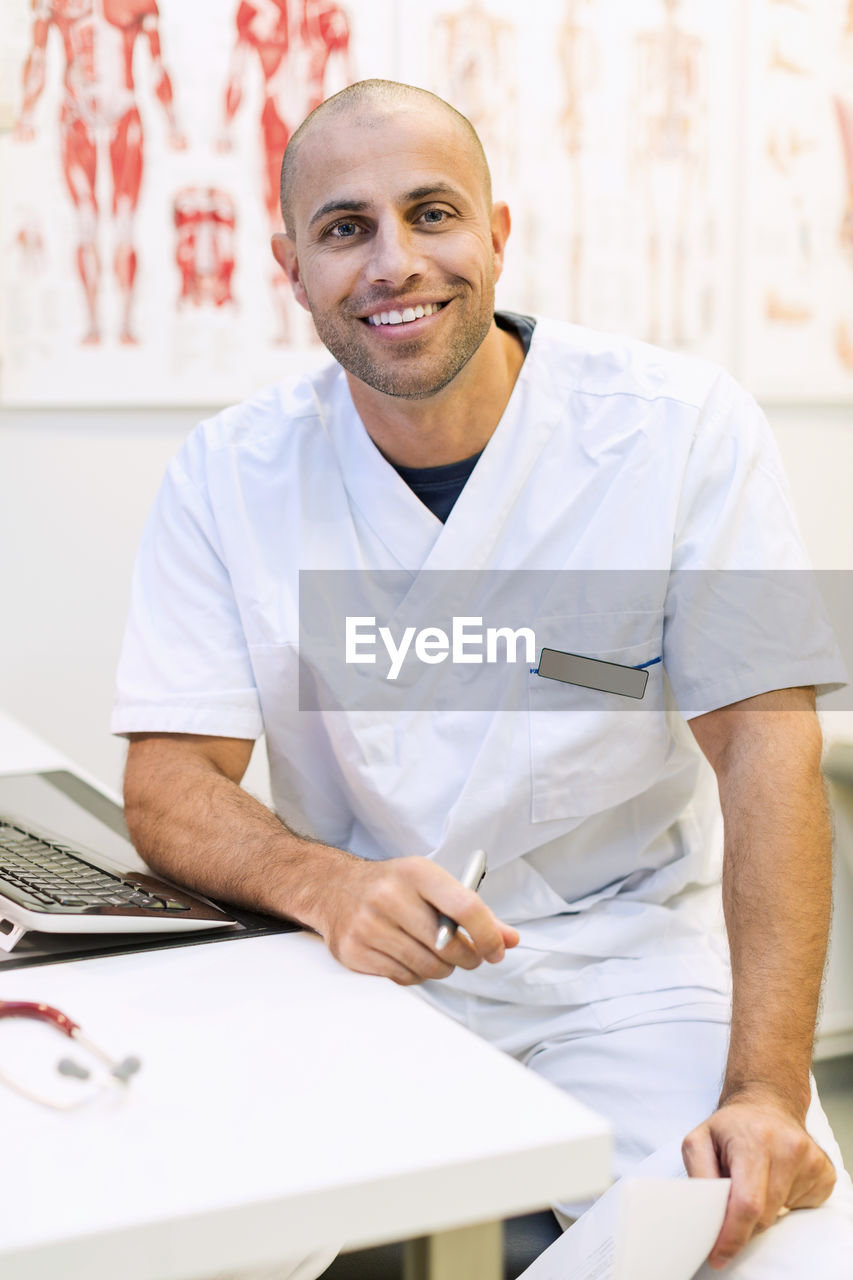 Portrait of happy male orthopedic doctor sitting at desk in clinic