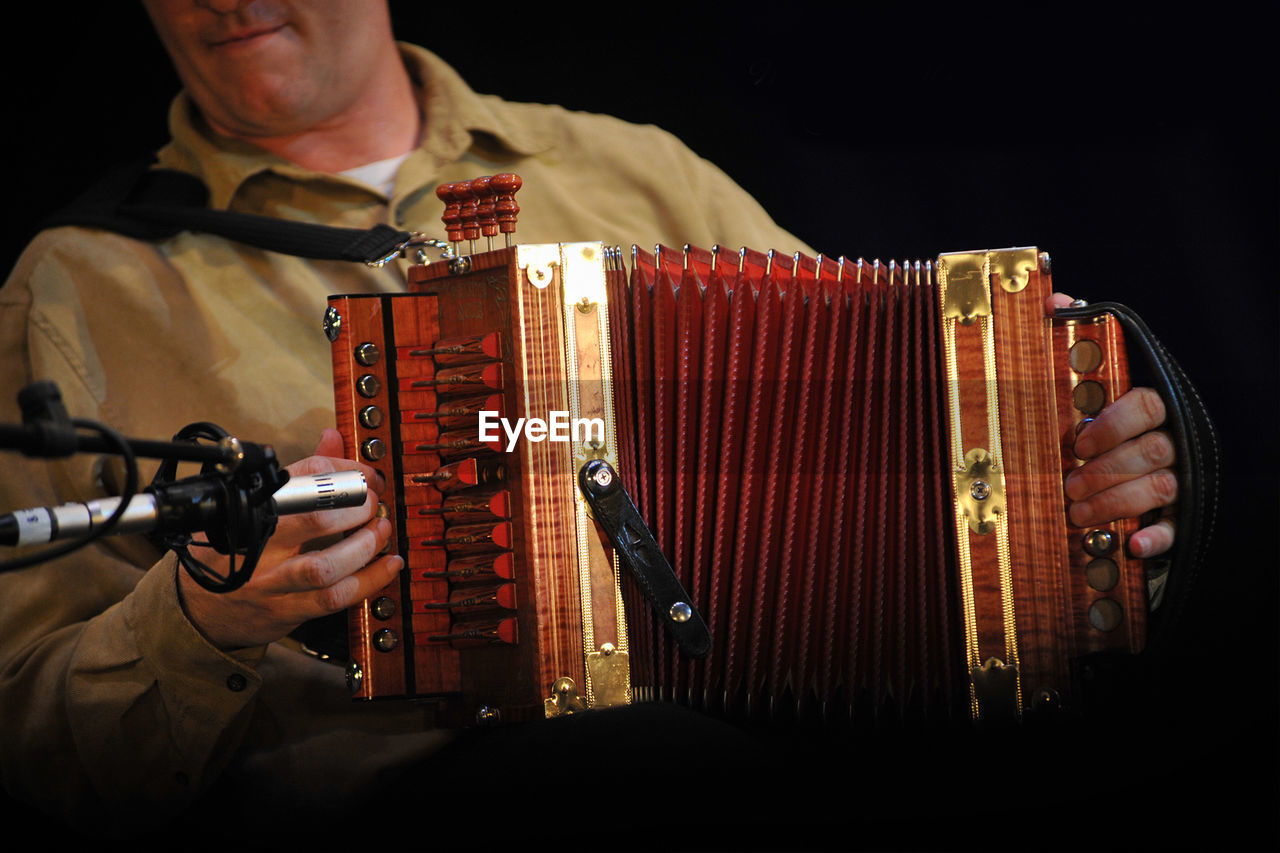 Midsection of musician playing accordion against black background