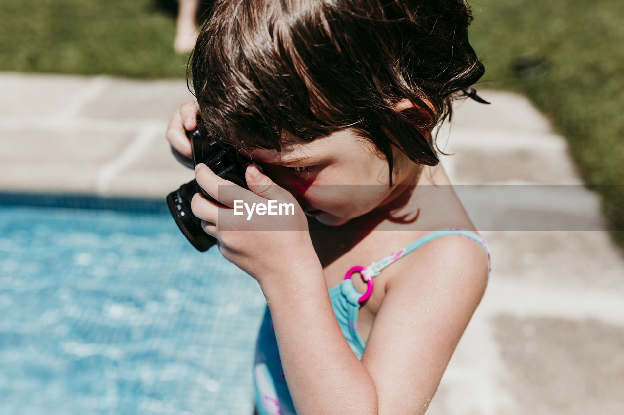 Side view of girl photographing by swimming pool