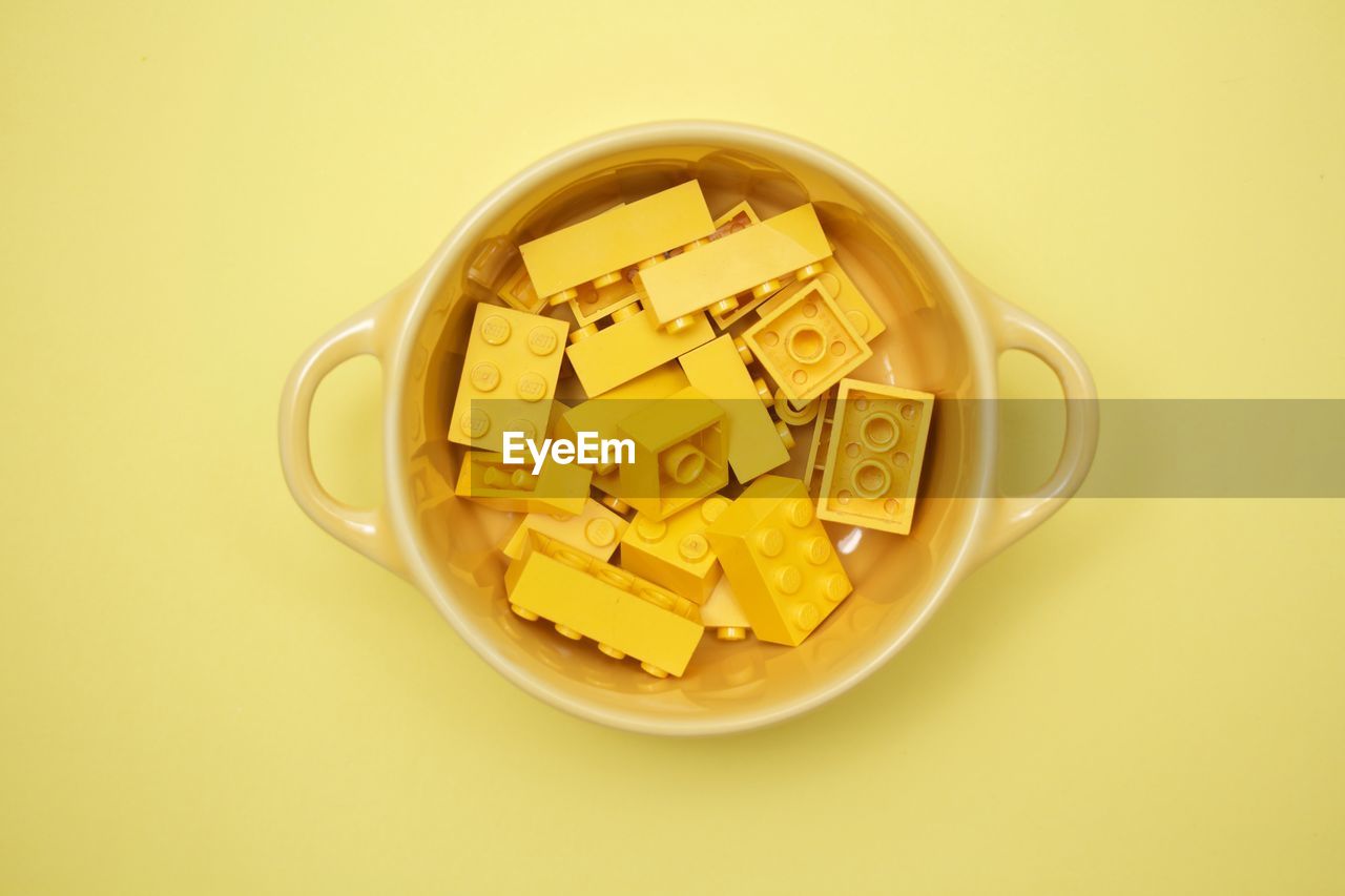 Directly above shot of toy blocks in bowl over yellow background