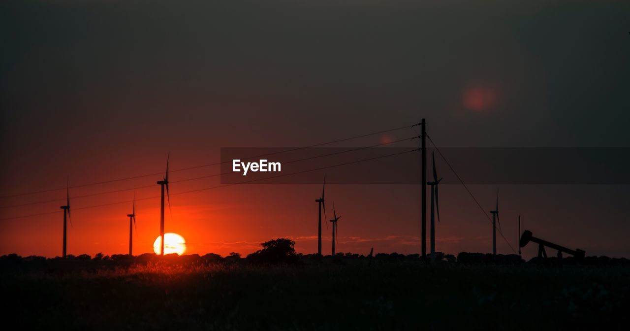 SILHOUETTE ELECTRICITY PYLONS ON FIELD AGAINST SKY AT SUNSET