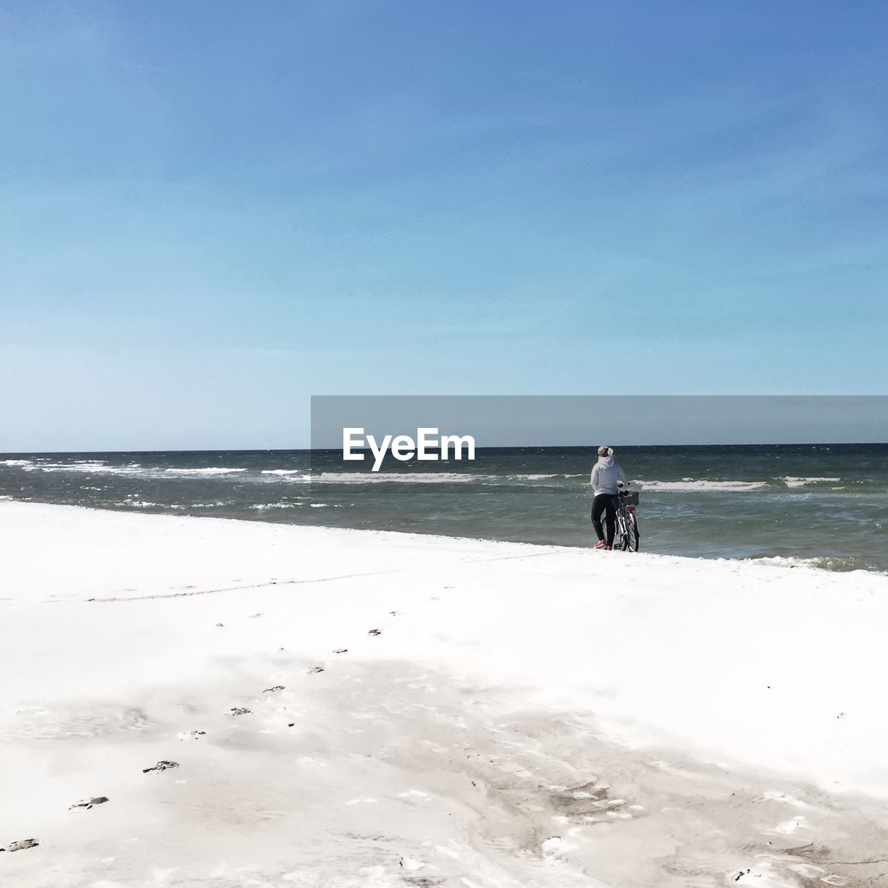 Woman walking with bicycle on beach against sky