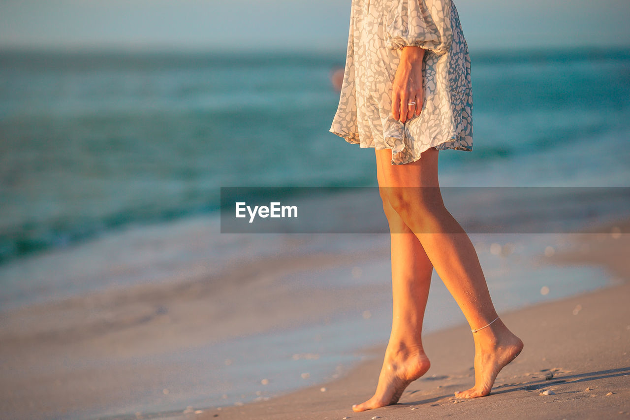 low section of woman standing on sand at beach