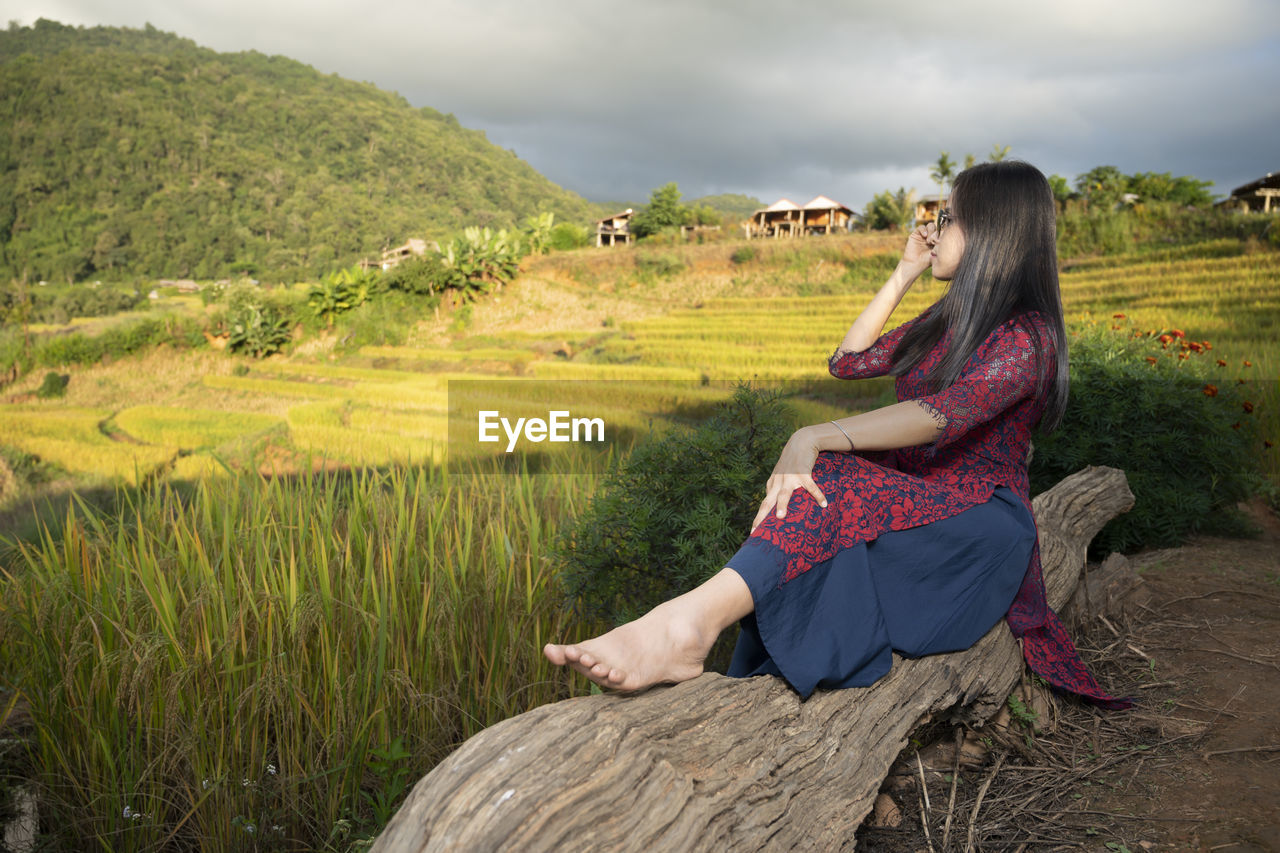 REAR VIEW OF WOMAN SITTING ON FARM