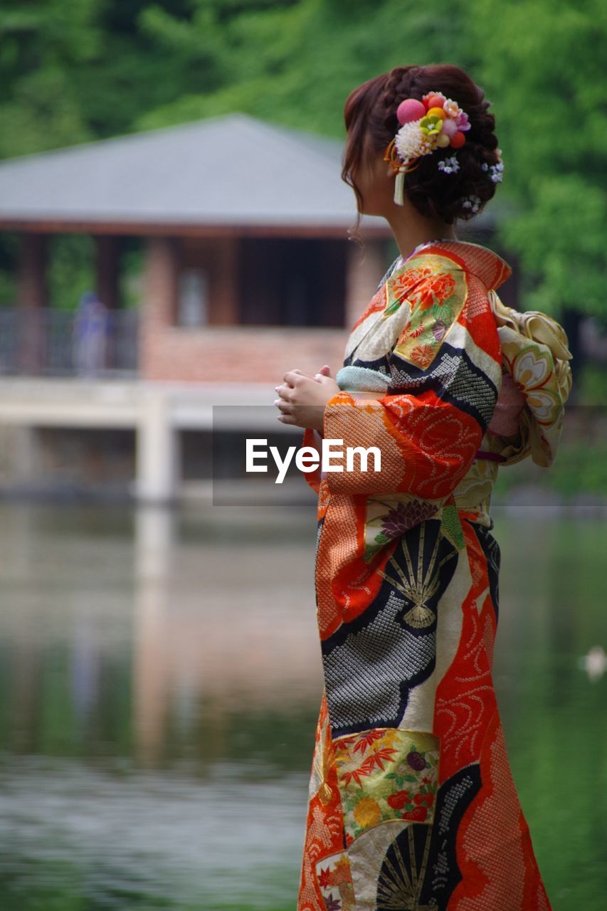 Side view of woman wearing traditional clothing standing at lakeshore