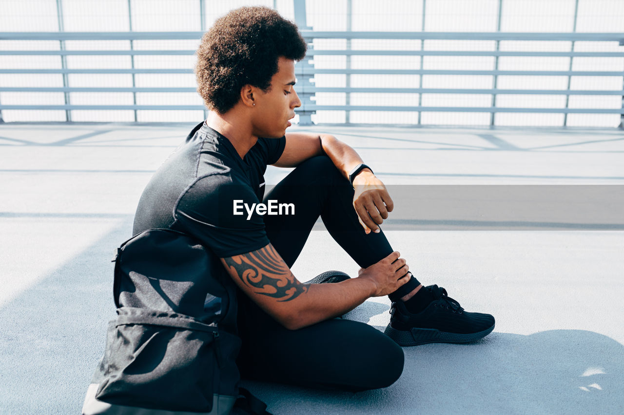 Side view of young man sitting on bridge