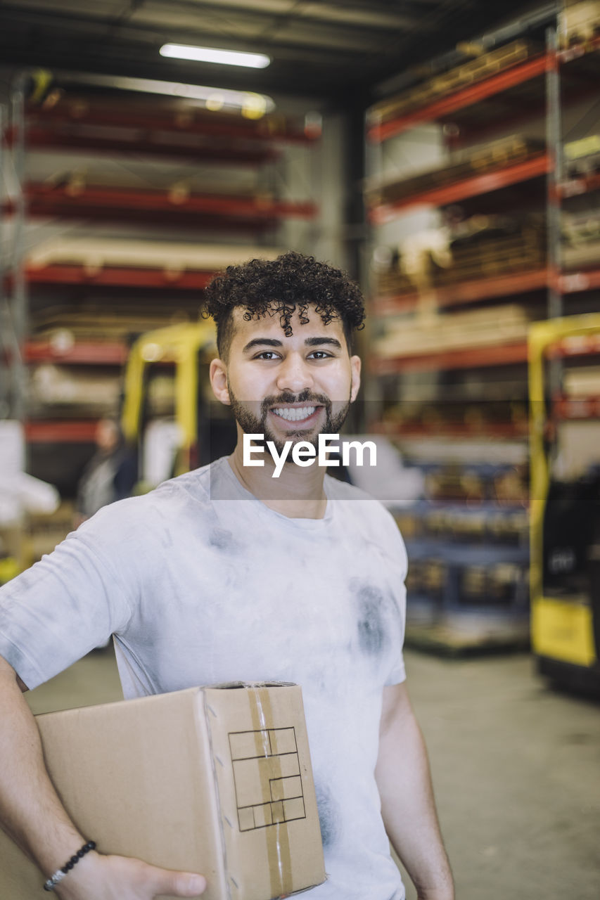 Portrait of happy young male carpenter with cardboard in warehouse