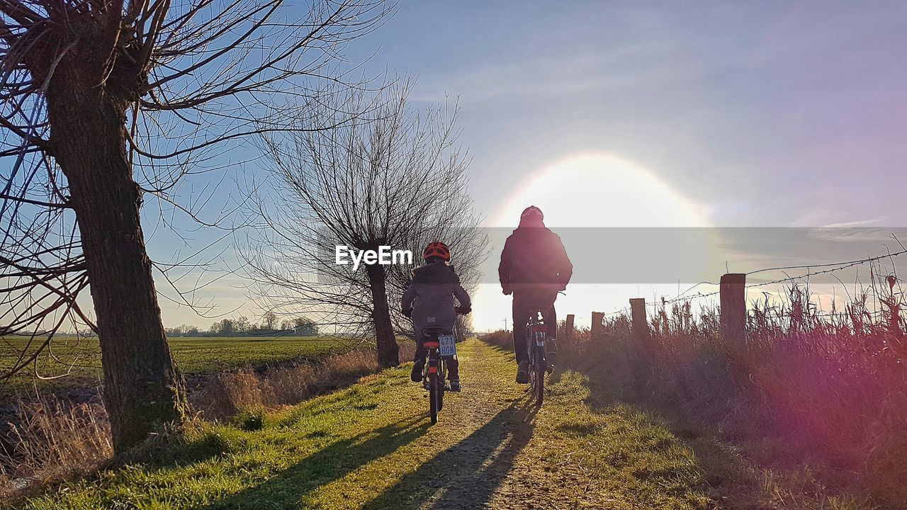 REAR VIEW OF PEOPLE RIDING BICYCLE ON FIELD