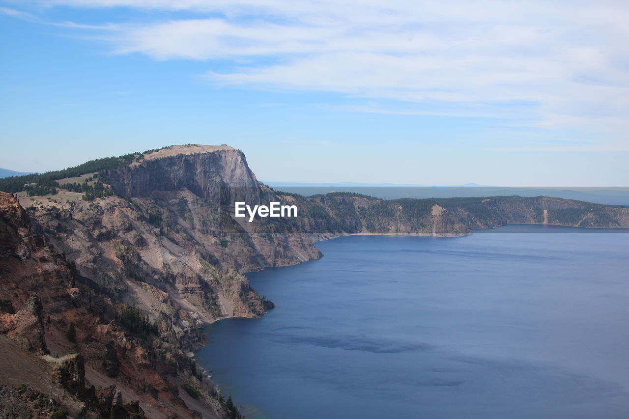 Scenic view of crater lake by cliff against sky