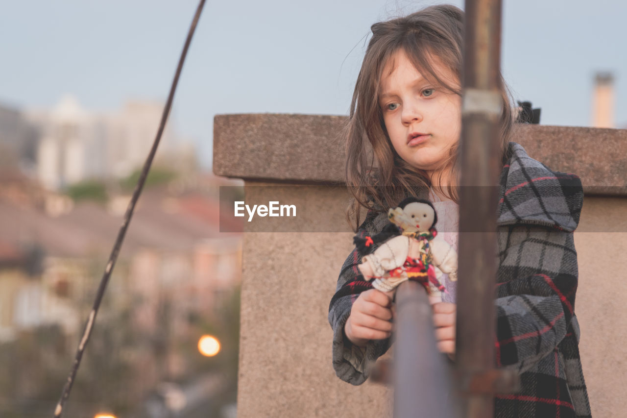 Thoughtful girl holding toy on railing in balcony