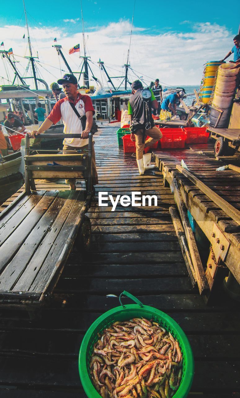 PEOPLE WORKING ON BOAT AGAINST SKY IN WATER