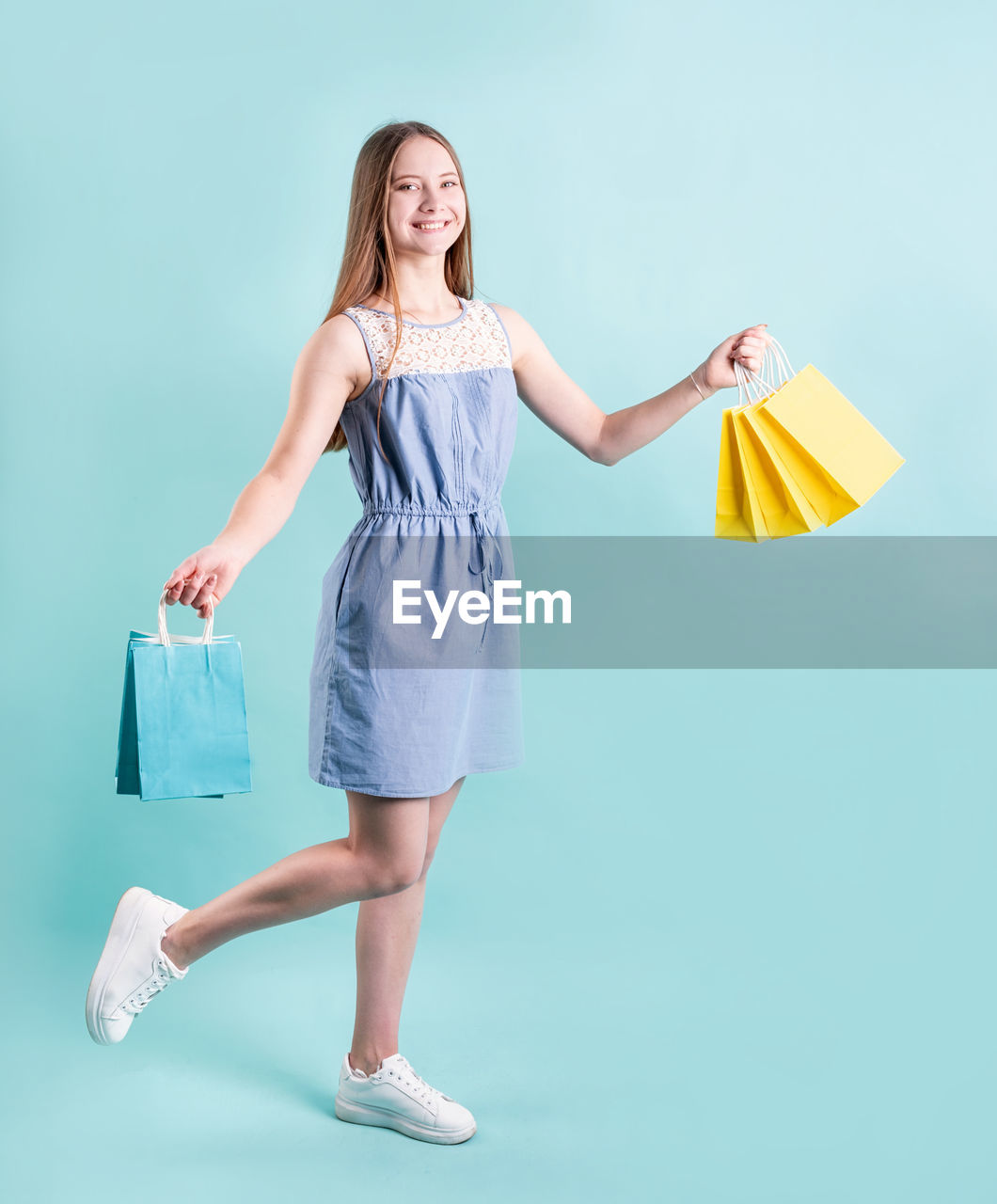 Shopping woman smiling. female teenager holding paper shopping bags isolated on blue background