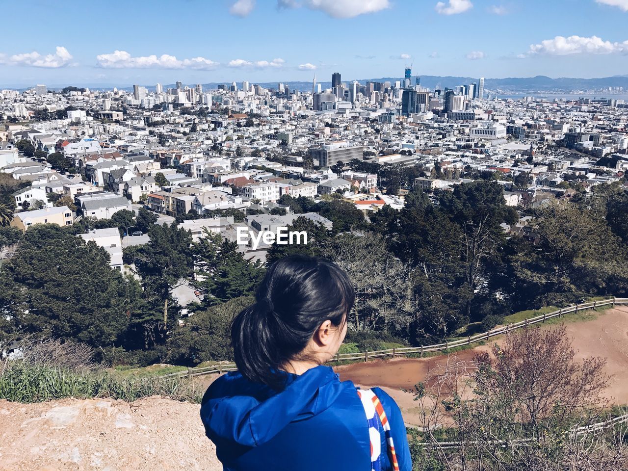 Rear view of woman standing on cliff while looking at cityscape