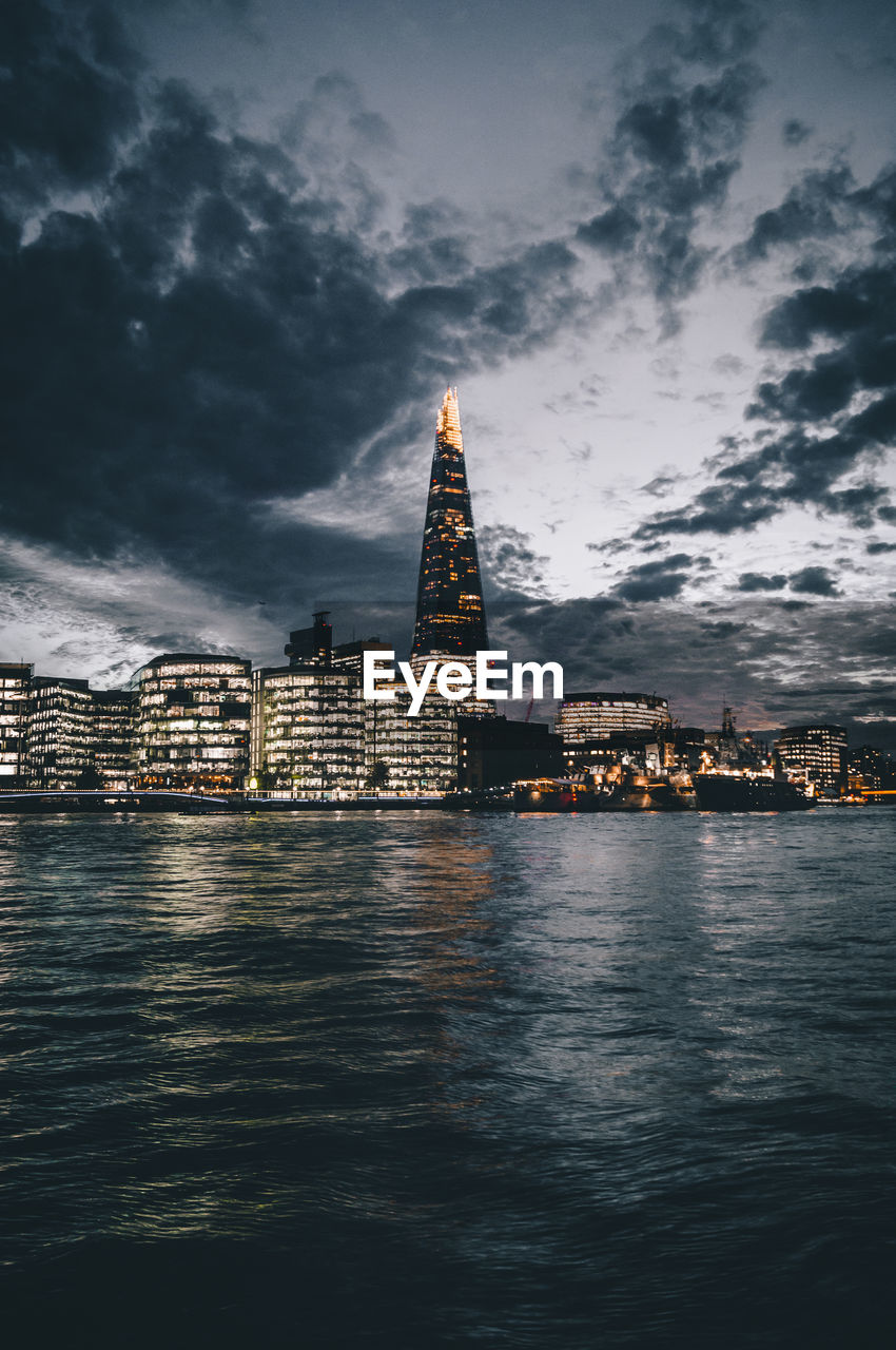 View of city at waterfront against cloudy sky