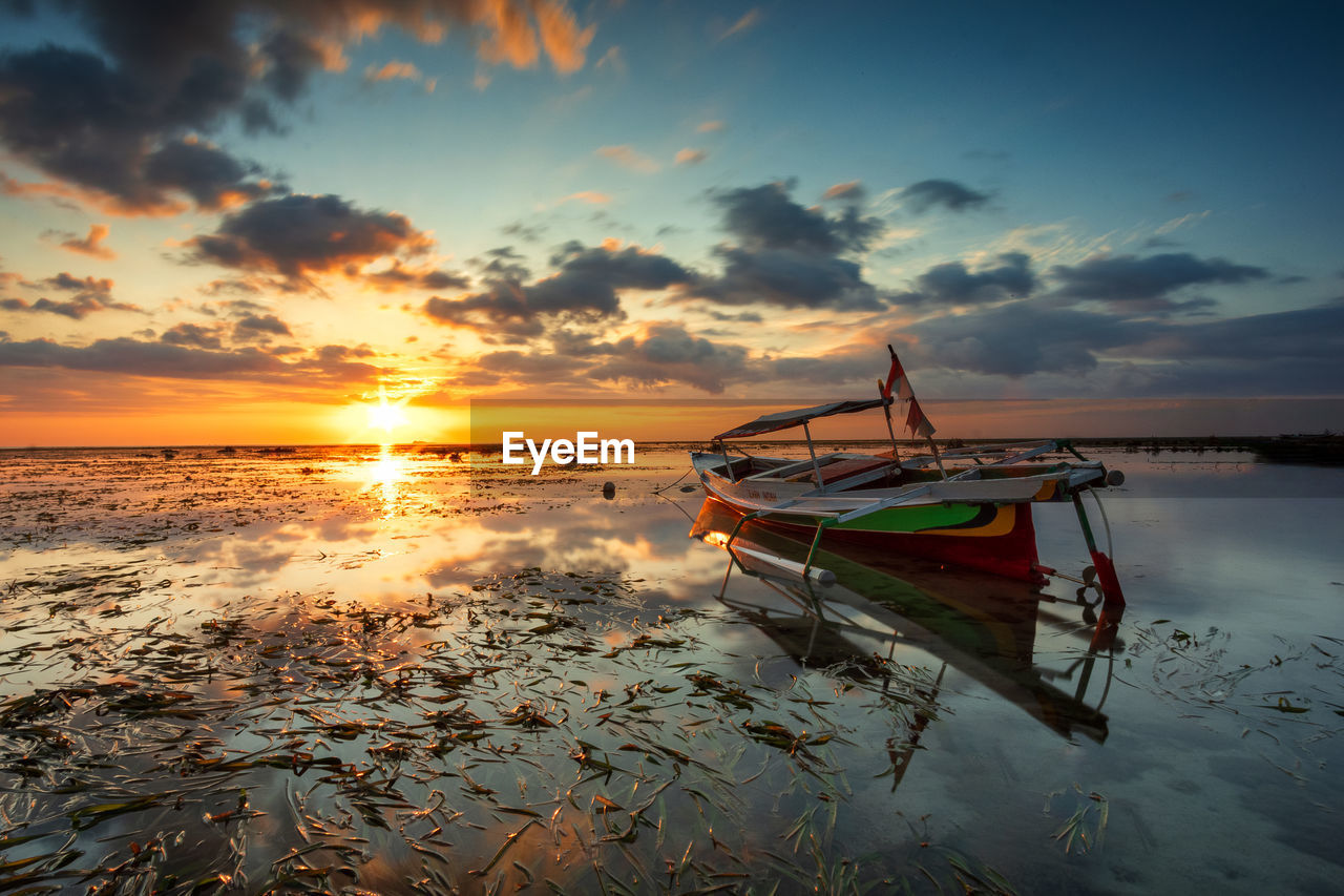 Boat moored at beach against sky during sunset
