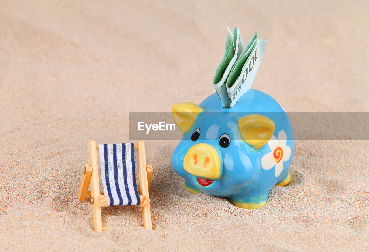 Close-up of piggy bank with paper currencies on sand