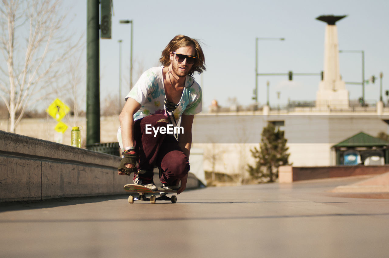 Man in sunglasses skateboarding on footpath