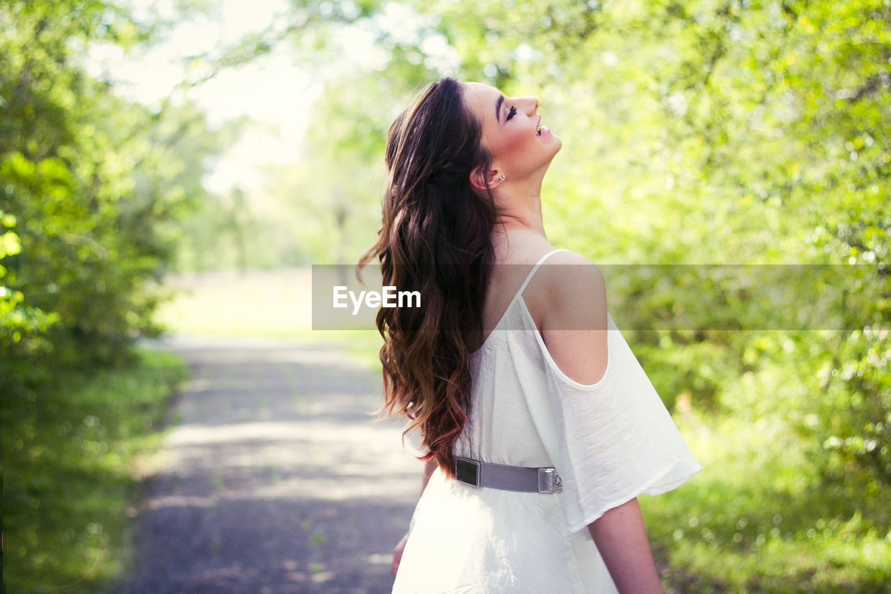 Smiling beautiful woman standing on footpath amidst trees