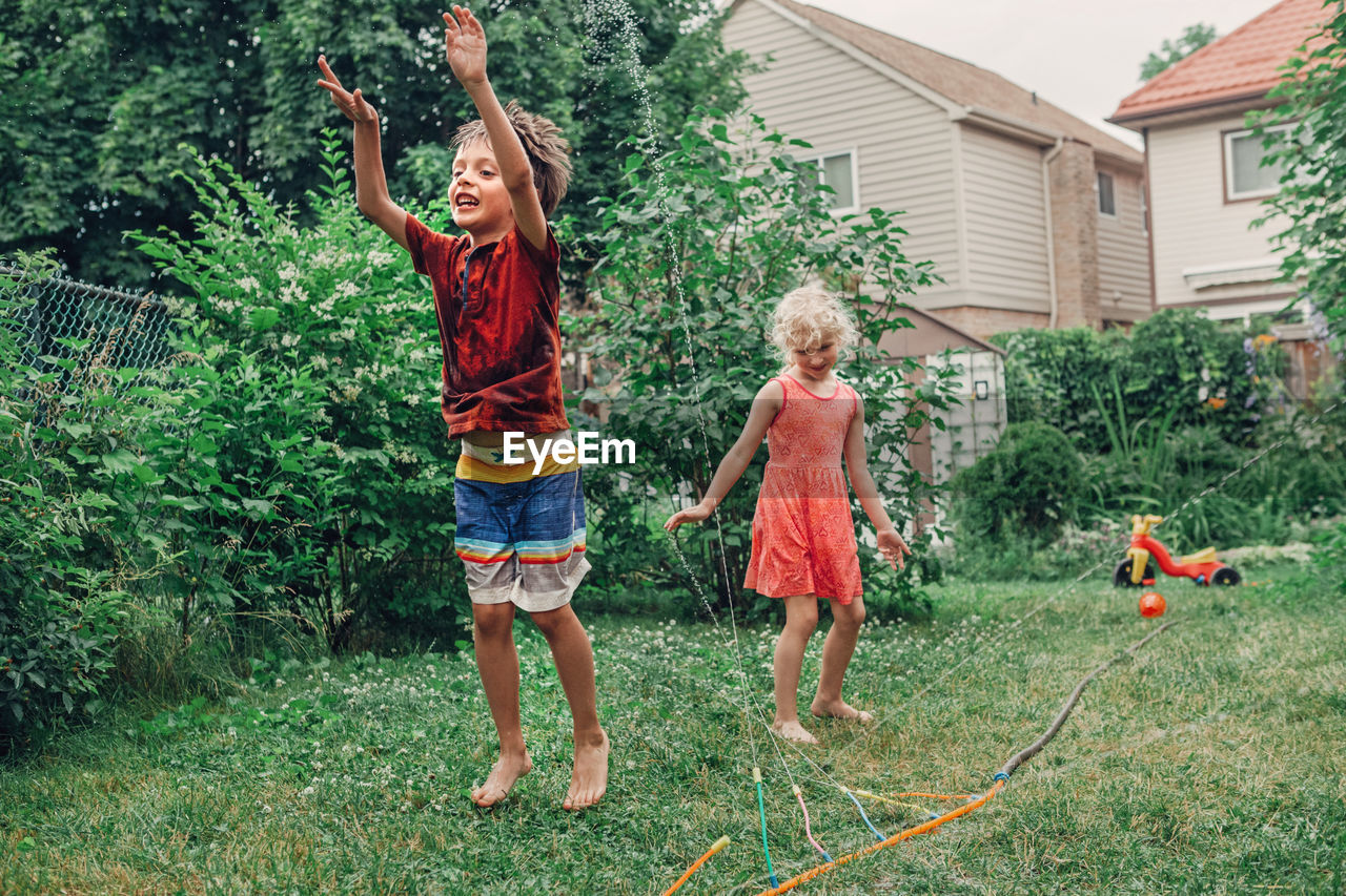 Siblings playing with sprinkler at yard