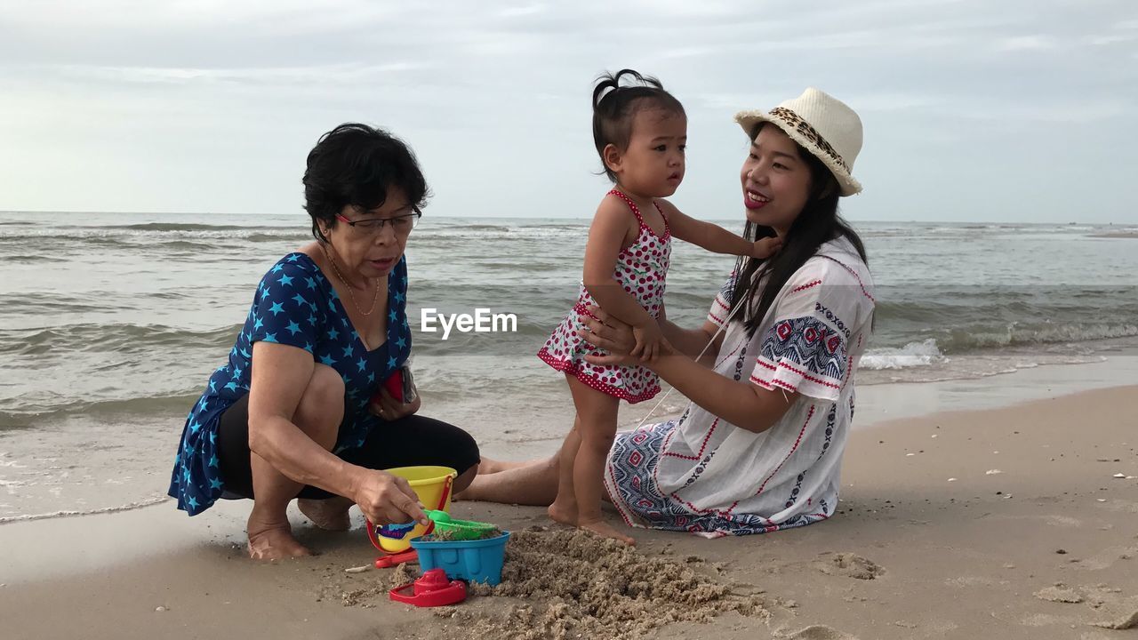 Smiling mother sitting with baby girl playing on shore at beach