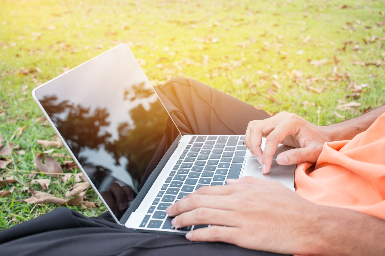 Midsection of man using laptop while sitting on grassy field