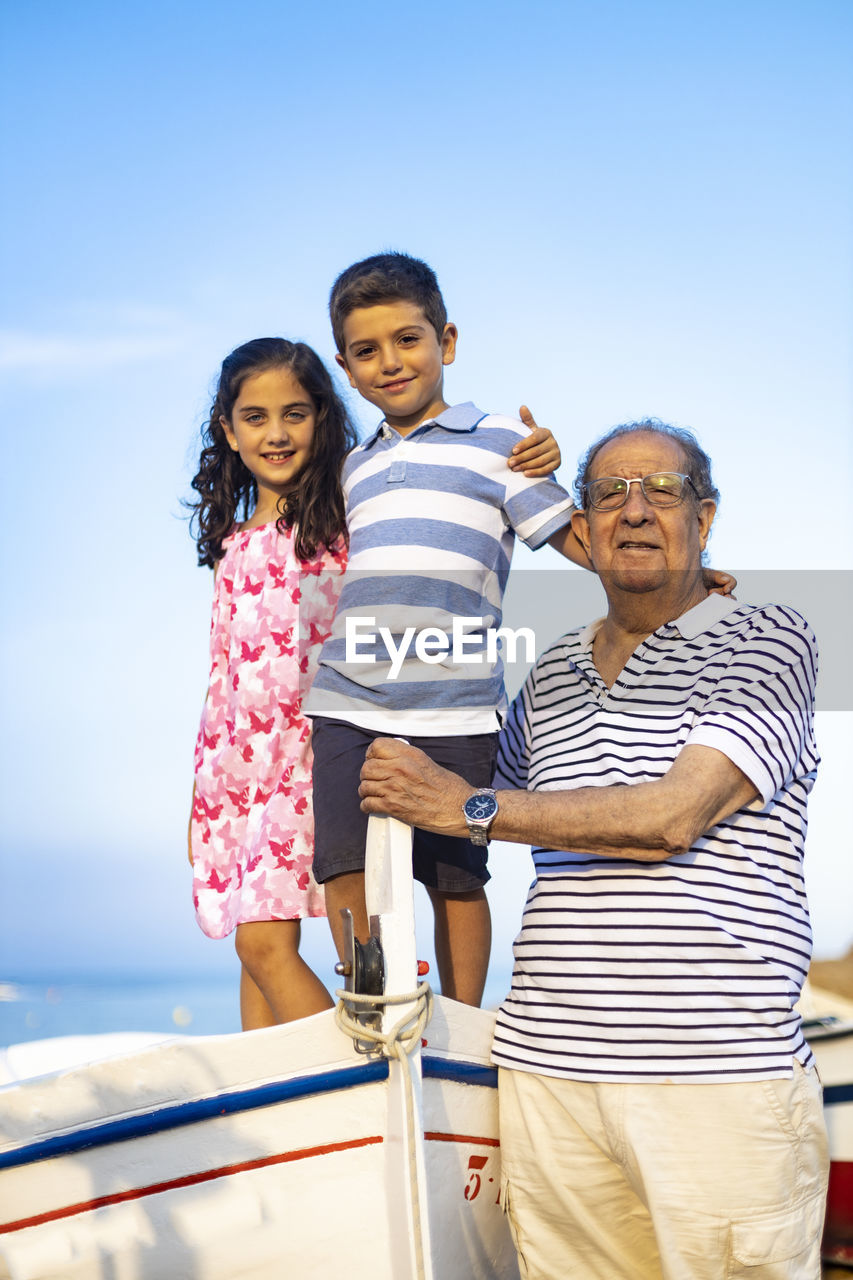 Grandfather with grandchildren on boat against sky