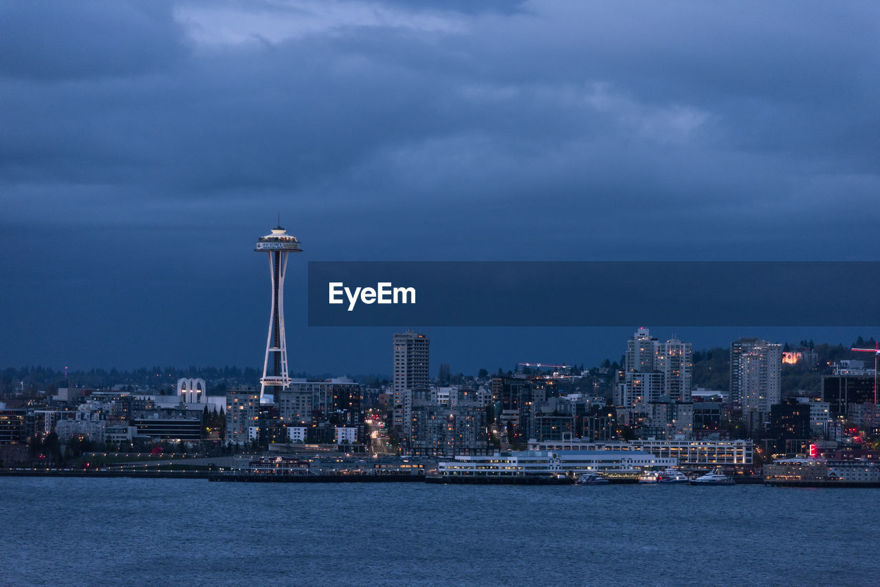 Illuminated buildings in city against cloudy sky