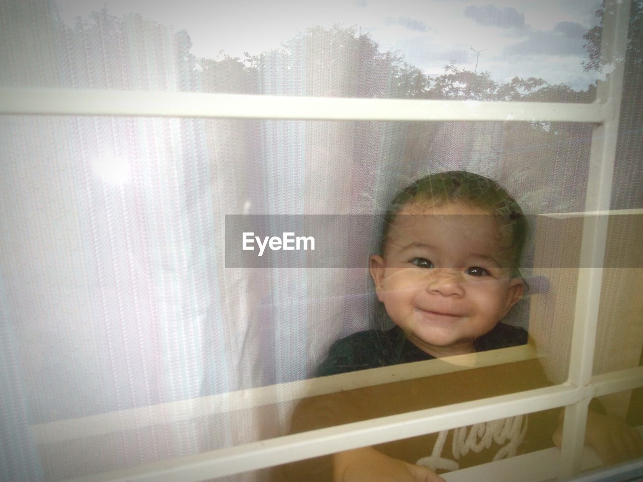 Portrait of cute smiling baby girl seen through window