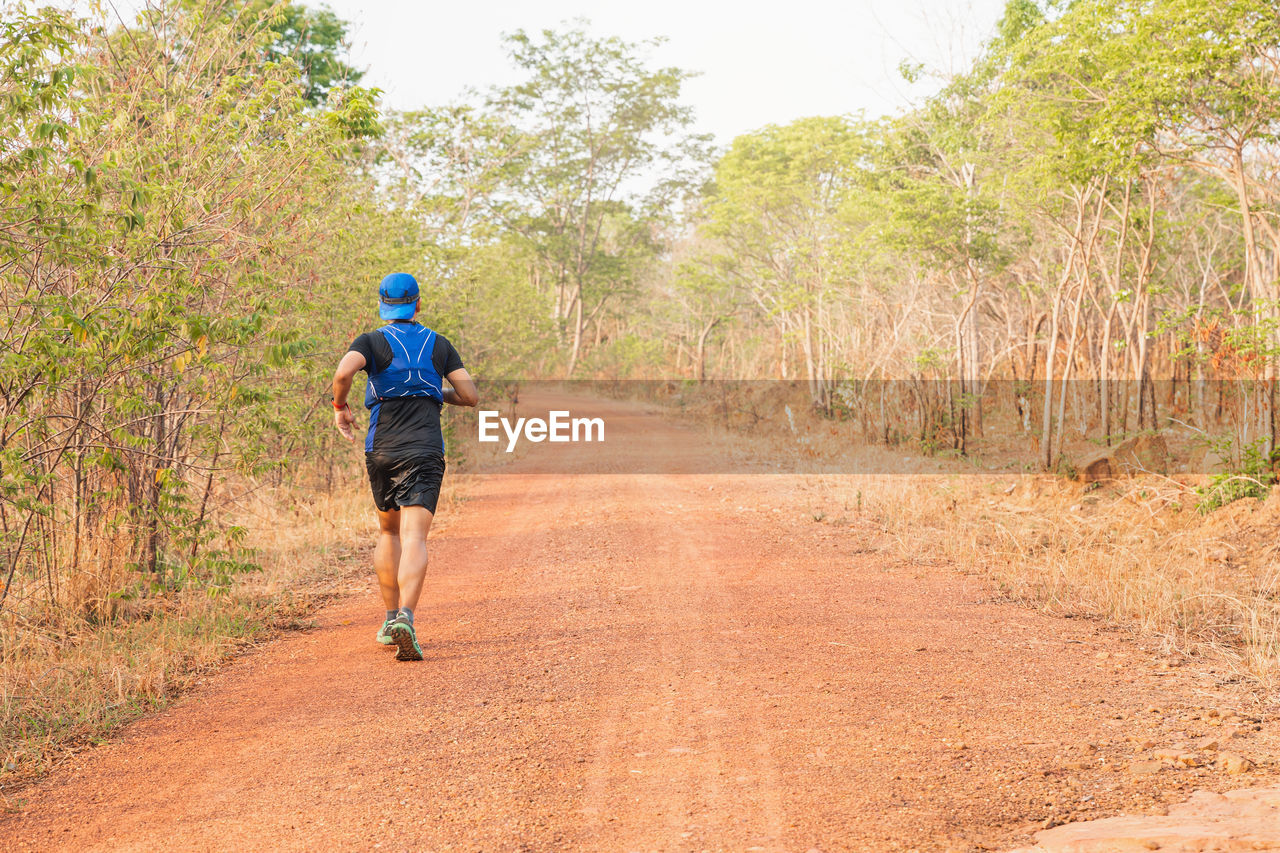 REAR VIEW OF MAN WALKING ON FOOTPATH